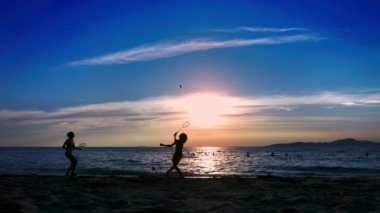 siluetleri. insanlar gün batımında sahilde badminton oynamak.