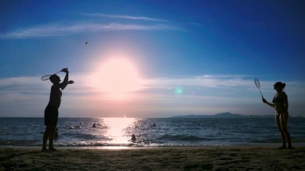 Siluetas. la gente juega bádminton en la playa al atardecer . — Vídeos de Stock
