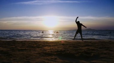 gün batımında, deniz, ince uzun bacaklı kız deniz kıyısında jimnastik darbeler yapıyor komik çerçevede bir kız silüeti