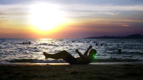 Verspielter, gutaussehender Typ in kurzen Hosen, der Fitness macht, am Strand vor der Kulisse eines wunderbaren Sonnenuntergangs — Stockvideo