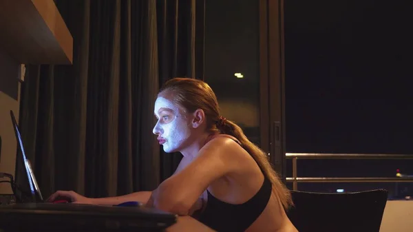 Wanita muda dengan topeng kosmetik pada wajah Bekerja dengan laptop di rumah di malam hari. kealamian — Stok Foto