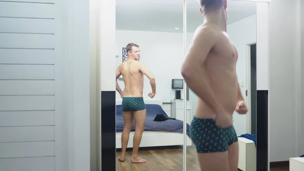 Młody człowiek sprawdzanie jego mięśnie przed lustrem w sypialni — Zdjęcie stockowe