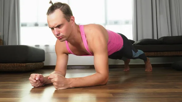 在他家的客厅里, 穿着粉色 t恤从事健身工作的有趣的帅哥. — 图库照片