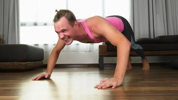 Игривый красавчик в розовой футболке занимается фитнесом, в гостиной своего дома . — стоковое фото