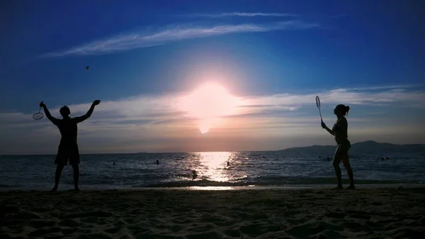 Sylwetki. ludzie grają w badmintona na plaży o zachodzie słońca. — Zdjęcie stockowe