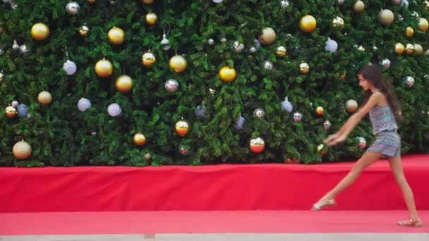 Happy girl doing gymnastic somersault on the background of the Christmas tree and palm trees in a tropical city. The concept of New Years travel to warm countries. — Stock Video