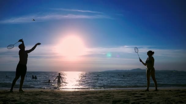 Siluetas. la gente juega bádminton en la playa al atardecer . — Vídeo de stock