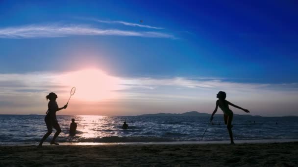 Siluetas. la gente juega bádminton en la playa al atardecer . — Vídeo de stock