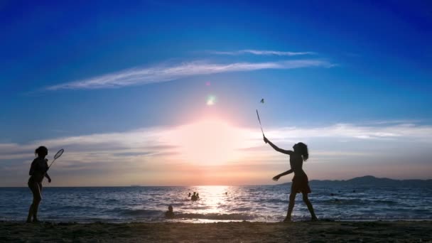 Silhouettes. les gens jouent au badminton sur la plage au coucher du soleil . — Video