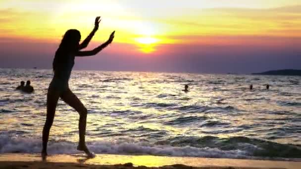 Силуэт девушки на закате, на фоне моря, стройная длинноногая девушка смешно делает гимнастические перевороты на морском побережье — стоковое видео