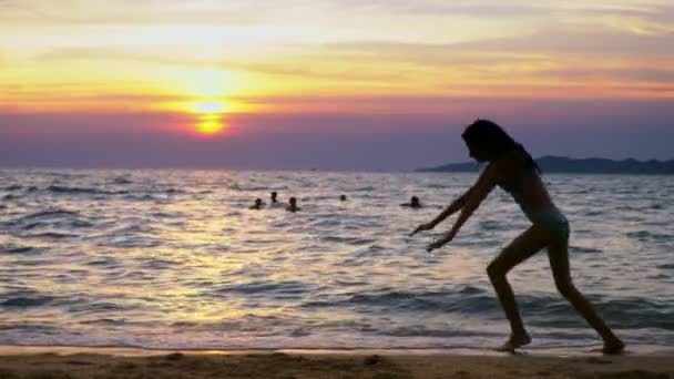 Silhouette of a girl at sunset, against the background of the sea, slender leggy girl funny doing gymnastic coups on the sea coast — Stock Video