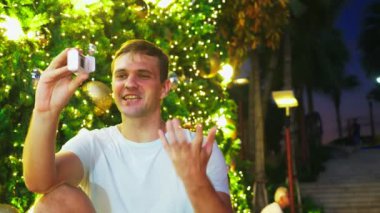 Noel ağacı ve palmiye ağaçları tropikal bir şehirde arka plan üzerinde mutlu bir adam. Yeni yıl kavramı sıcak ülkelere seyahat. telefonu kullanma