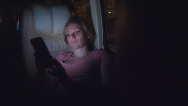 Een vermoeide vrouw rijdt de nacht op de bus, gebruik maken van haar telefoon. — Stockvideo
