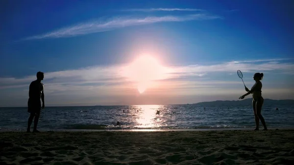 Silhouetten. Menschen spielen Badminton am Strand bei Sonnenuntergang. — Stockfoto