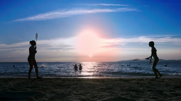 Silhouetten. Menschen spielen Badminton am Strand bei Sonnenuntergang. — Stockfoto