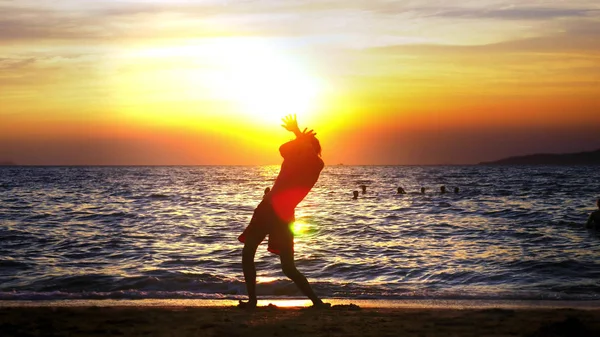 Silueta de un niño en el fondo de la puesta de sol del mar, divertido adolescente bailando en el fondo de una puesta de sol en el mar — Foto de Stock