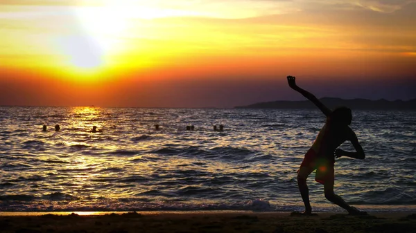 Silhueta de um menino no fundo do pôr-do-sol do mar, engraçado adolescente dançando no fundo de um pôr-do-sol no mar — Fotografia de Stock