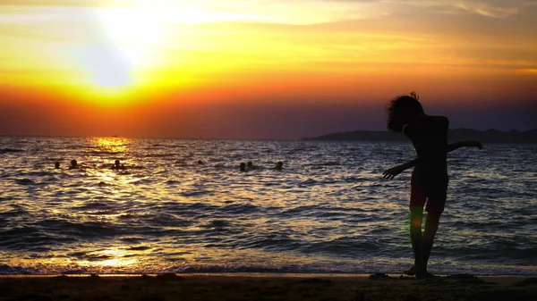 Silhueta de um menino no fundo do pôr-do-sol do mar, engraçado adolescente dançando no fundo de um pôr-do-sol no mar — Fotografia de Stock