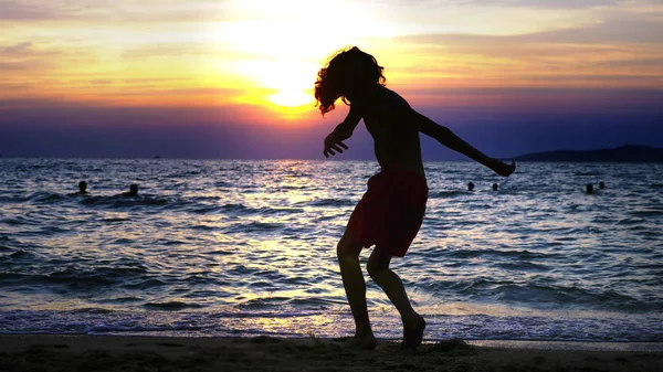 剪影一个男孩在海日落的背景, 滑稽的少年男孩在日落的背景下跳舞在海的背景下 — 图库照片