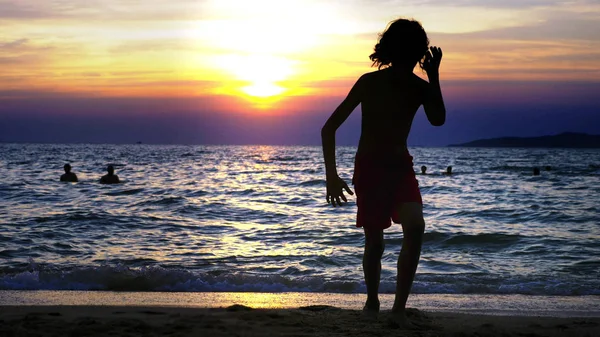 剪影一个男孩在海日落的背景, 滑稽的少年男孩在日落的背景下跳舞在海的背景下 — 图库照片