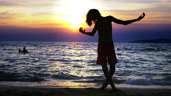 Silhueta de um menino no fundo do pôr-do-sol do mar, engraçado adolescente dançando no fundo de um pôr-do-sol no mar — Fotografia de Stock