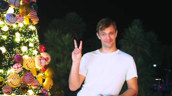 Homem feliz no fundo da árvore de Natal e palmeiras em uma cidade tropical. O conceito de viagens de Ano Novo a países quentes . — Fotografia de Stock