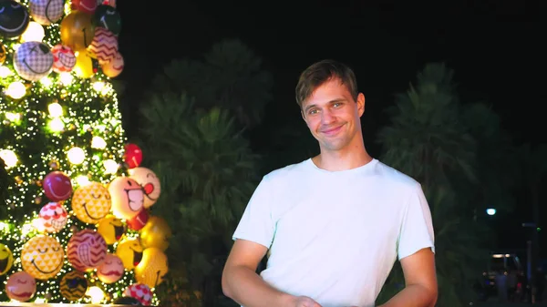 Hombre feliz en el fondo del árbol de Navidad y palmeras en una ciudad tropical. El concepto de Año Nuevo viaja a países cálidos . — Foto de Stock