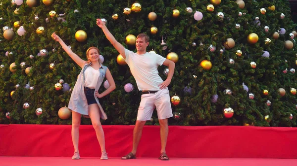 Ein glückliches Paar tanzt auf dem Hintergrund des Weihnachtsbaums in einer tropischen Stadt. das Konzept der Neujahrsreisen in warme Länder. — Stockfoto