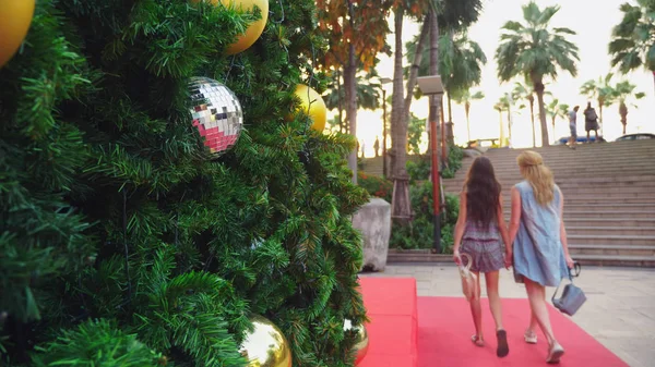 Mãe feliz e filha no fundo da árvore de Natal em uma cidade tropical. O conceito de viagens de Ano Novo a países quentes . — Fotografia de Stock