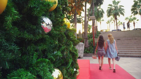 Mãe feliz e filha no fundo da árvore de Natal em uma cidade tropical. O conceito de viagens de Ano Novo a países quentes . — Fotografia de Stock