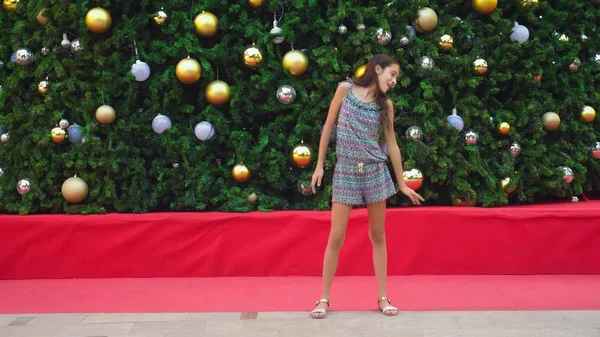 Fröhliches Mädchen, das auf dem Hintergrund von Weihnachtsbaum und Palmen in einer tropischen Stadt tanzt. das Konzept der Neujahrsreisen in warme Länder. — Stockfoto