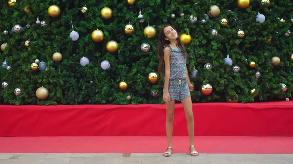 Chica feliz haciendo voltereta gimnástica en el fondo del árbol de Navidad y palmeras en una ciudad tropical. El concepto de Año Nuevo viaja a países cálidos . — Foto de Stock