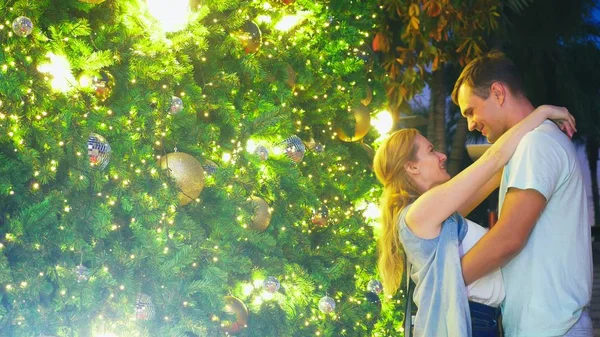 Happy couple meet new year on the background of the Christmas tree in a tropical city. congratulations and kisses. The concept of New Years travel to warm countries — Stock Photo, Image