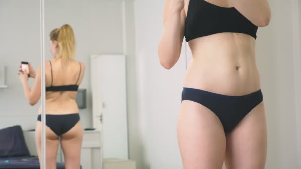 Η έννοια του υπερβολικού βάρους και απώλεια βάρους. Μια γυναίκα κοιτάζει τον εαυτό της στον καθρέφτη και φωτογραφίες το σχήμα της. να συγκρίνετε τα αποτελέσματα πριν και μετά την απώλεια βάρους. — Αρχείο Βίντεο