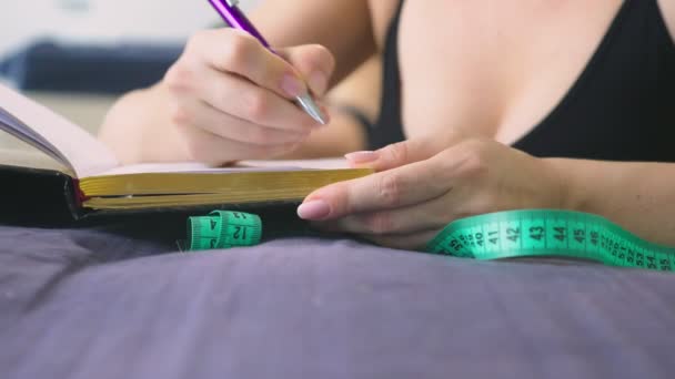 Het concept van overgewicht en gewichtsverlies. Een vrouw zelf maatregelen met een meetlint in de slaapkamer, kijken naar zichzelf in de spiegel, en schrijft de resultaten naar een notitieblok — Stockvideo