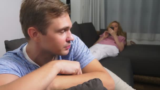 Paarkrise. Mann und Frau verbringen den Abend im Wohnzimmer auf der Couch. die Frau telefoniert, der Mann ärgert sich, dass sie nicht auf ihn achtet. — Stockvideo