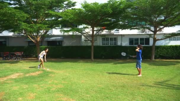 Хлопчик-підліток і дівчинка грають в бадмінтон на зеленому газоні на задньому дворі свого будинку — стокове відео