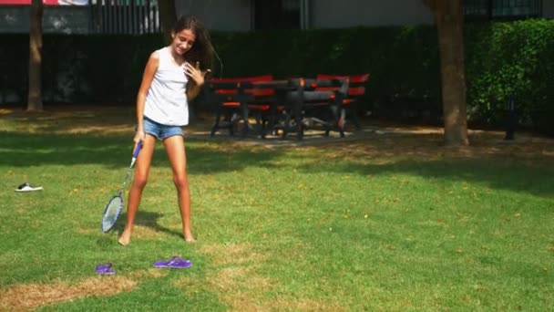 Un ragazzo adolescente e una ragazza giocano a badminton su un prato verde nel cortile della loro casa — Video Stock