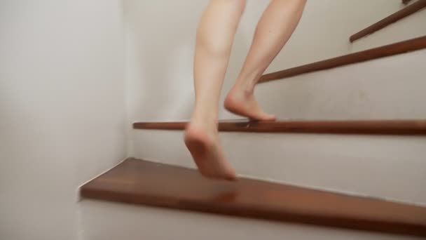 Gros plan. Les pieds des femmes montent les escaliers en bois. une femme en chemise homme monte à l'étage — Video