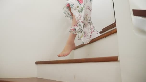 Close-up. Os pés descalços femininos descem as escadas de madeira. Uma mulher de saia comprida desce as escadas. detém sandálias castanhas — Vídeo de Stock