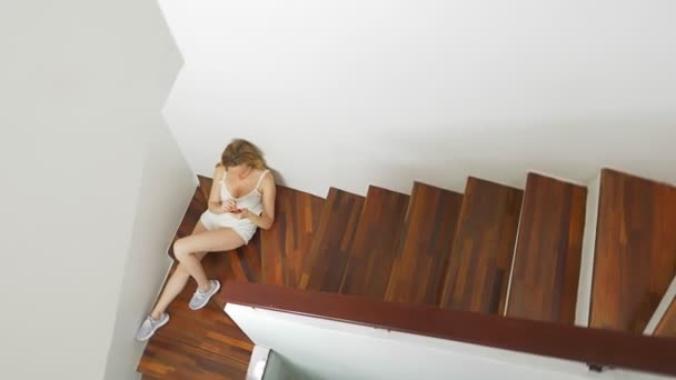 Dziewczyny w krótkich spodenkach siedzi na schodach w domu i używa smartfonu — Wideo stockowe