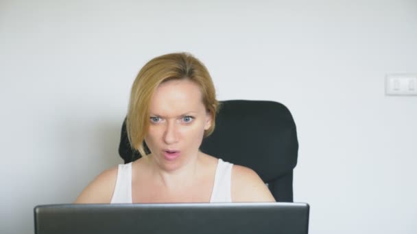 En kvinna med hennes laptop, sitter vid bordet, arg och irriterad, svär. Mänskliga känslor. Internet addiction koncept. — Stockvideo