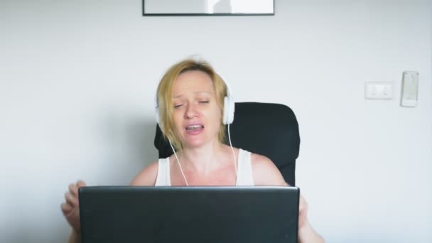 Una mujer que usa su portátil está sentada a la mesa, riendo y hablando. Emociones humanas. Adicción a Internet . — Vídeos de Stock