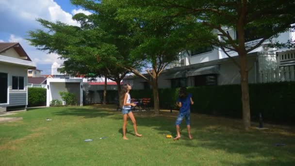 Un ragazzo adolescente e una ragazza giocano a badminton su un prato verde nel cortile della loro casa — Video Stock