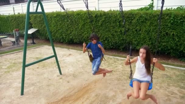 Мальчик и девочка-подросток качаются на качелях босыми ногами на зеленой лужайке на заднем дворе своего дома — стоковое видео