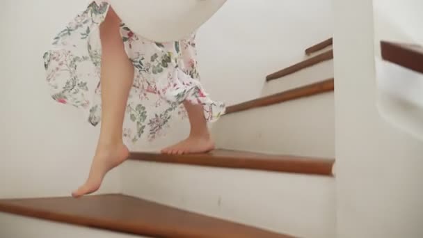 Primo piano. Le gambe nude femminili scendono le scale di legno. una donna con una bella gonna lunga cammina per le scale. tenendo un cappello da spiaggia a tesa larga — Video Stock