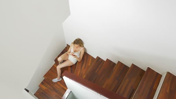 Chica en pantalones cortos se sienta en las escaleras en casa y utiliza un teléfono inteligente — Vídeo de stock