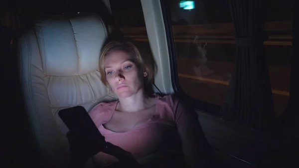 Seorang wanita lelah naik malam di bus, menggunakan teleponnya . — Stok Foto