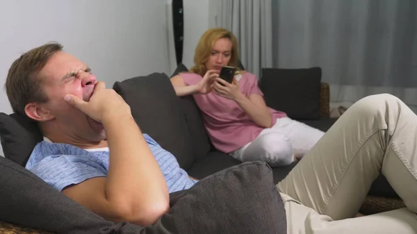 Пара проблем. Мужчина и женщина проводят вечер в гостиной на диване. женщина использует телефон, мужчина расстроен, что она не обращает на него внимания . — стоковое фото