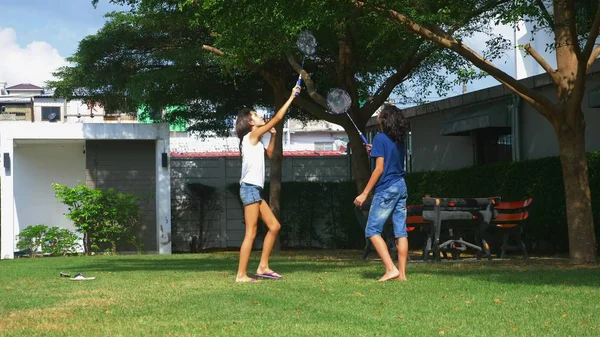 Un adolescent garçon et une fille jouent au badminton sur une pelouse verte dans la cour arrière de leur maison — Photo